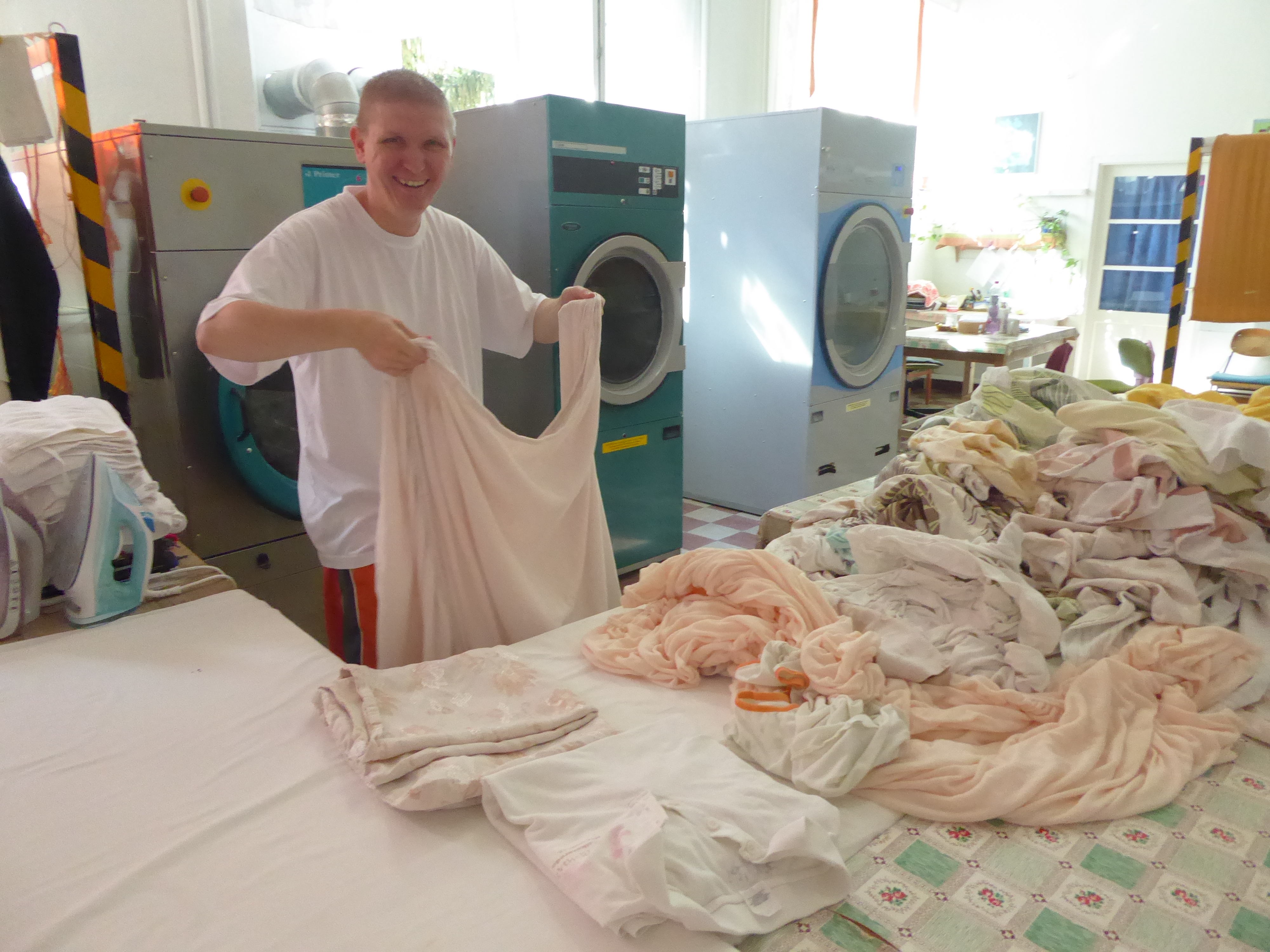 A fotón Erbeszkorn Zsolt látható, amint a mosodában dolgozik. A kép középpontjában Ő látható, mögötte három ipari mosógép. Előtte egy hosszú asztal a kimosott ruhaneműkkel, melyeket éppen hajtogat.