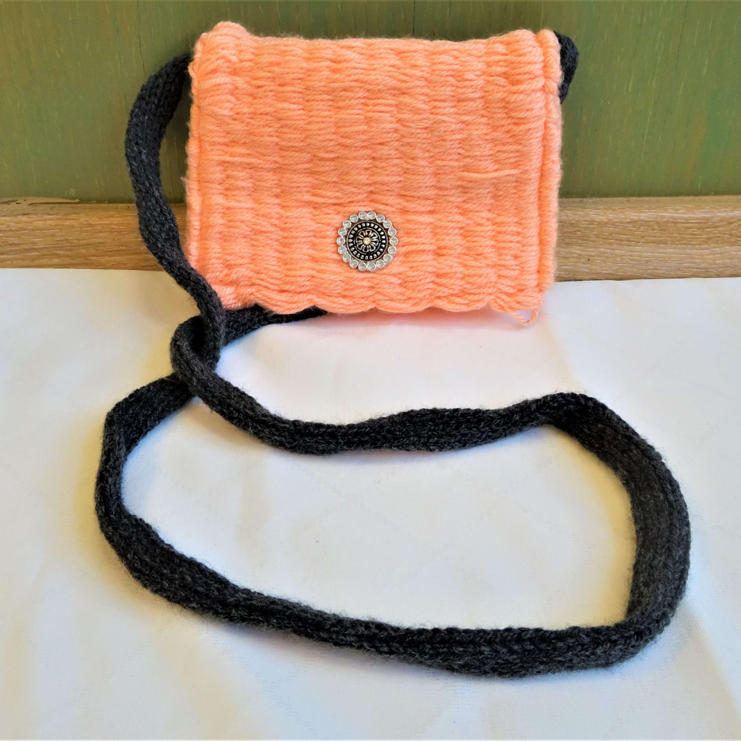A Tarisznya szövéssel készült puha, kisméretű szőttes, amely bélésanyaggal rendelkezik. A táska világos narancsszínű, amelyen fém díszgomb található, a fekete színű füle hosszú, ezáltal vállon hordható.