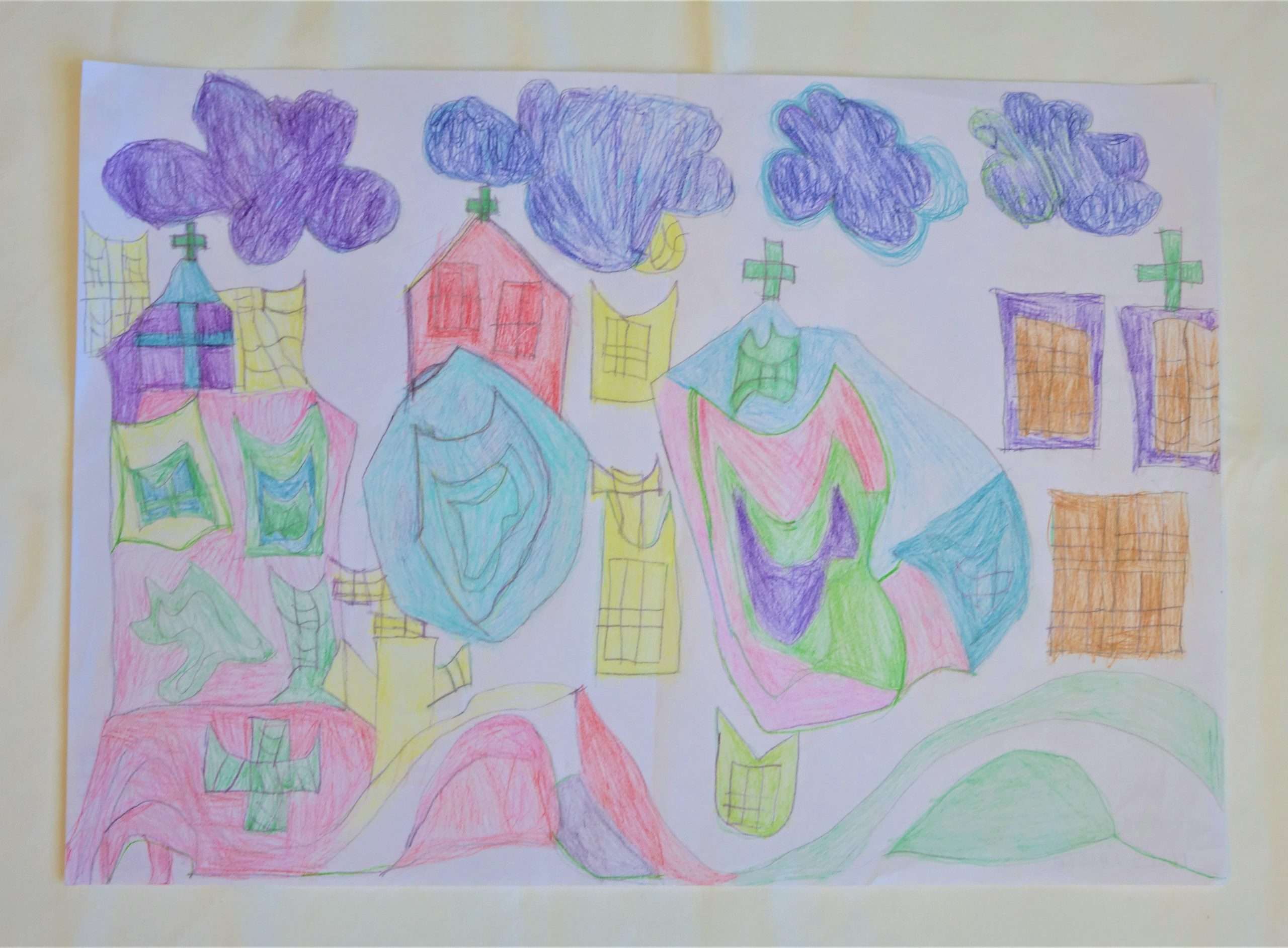 A színes ceruzákkal készített rajz kastélyokat ábrázol. A kastélyokon színes formák, tetejükön keresztek láthatók. A kép felső részén 4 kékes, lilás felhő úszik.