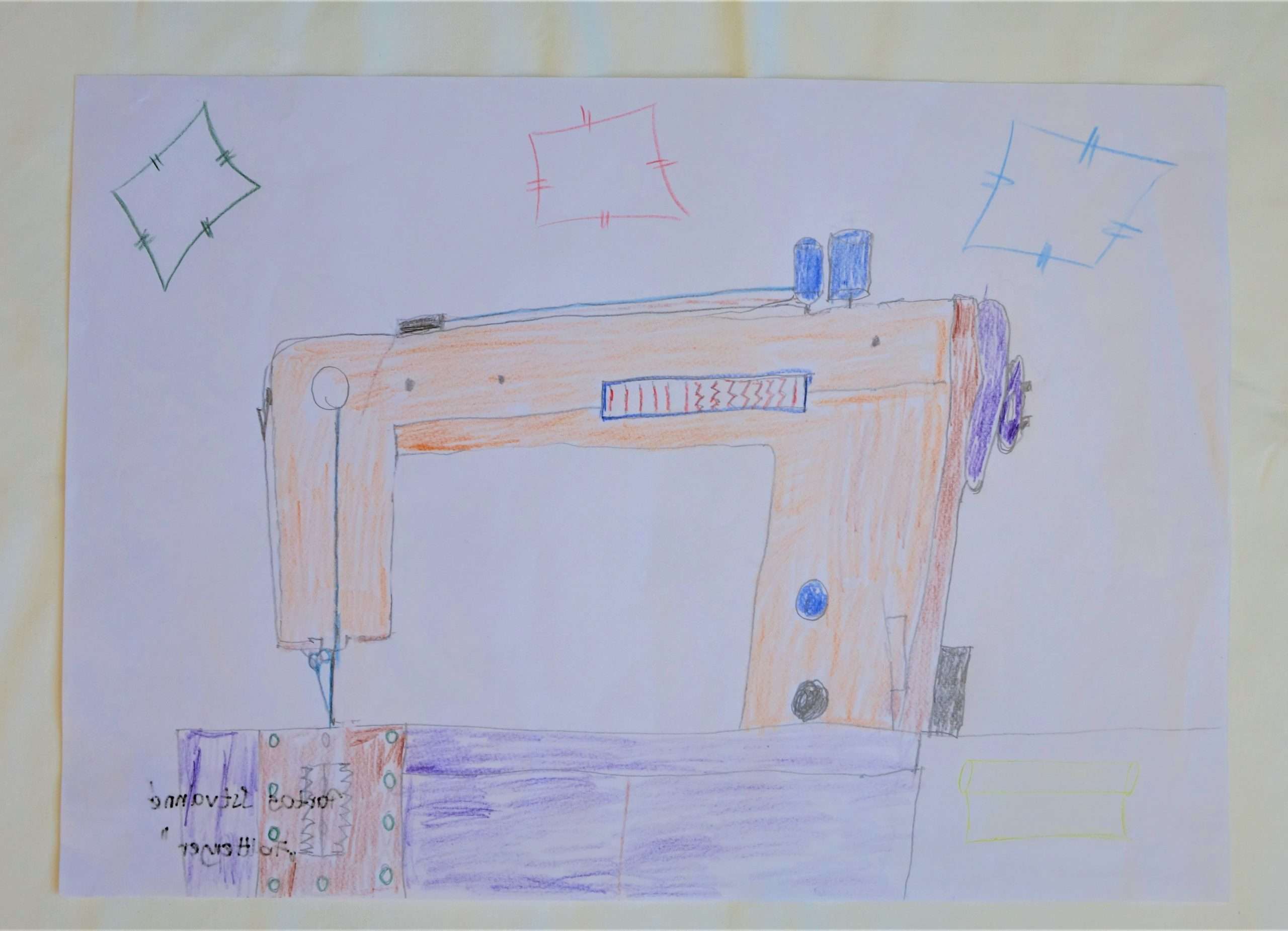 Színes ceruzával készített rajz, amely egy varrógépet ábrázol. A varrógép lila és narancssárga színekkel van kiszínezve. A kép felső részére 3 folt körvonalait rajzolta az alkotó.