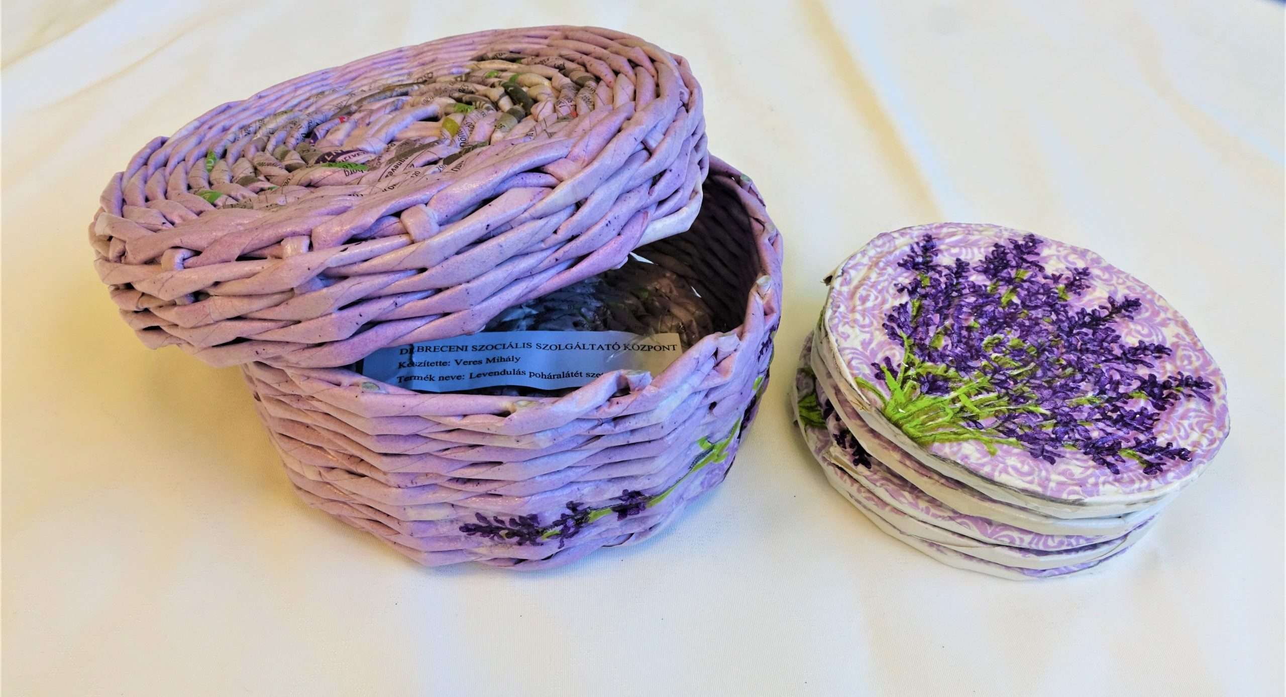 A Levendulás poháralátét szettben dobozban, egy papírból készült lila színű fedett kosár, benne 6 darab poháralátéttel, amelyre mintának levendulák kerültek szalvétatechnikával.